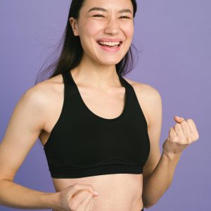 Portrait of a smiling young woman in black sportswear against a purple background.
